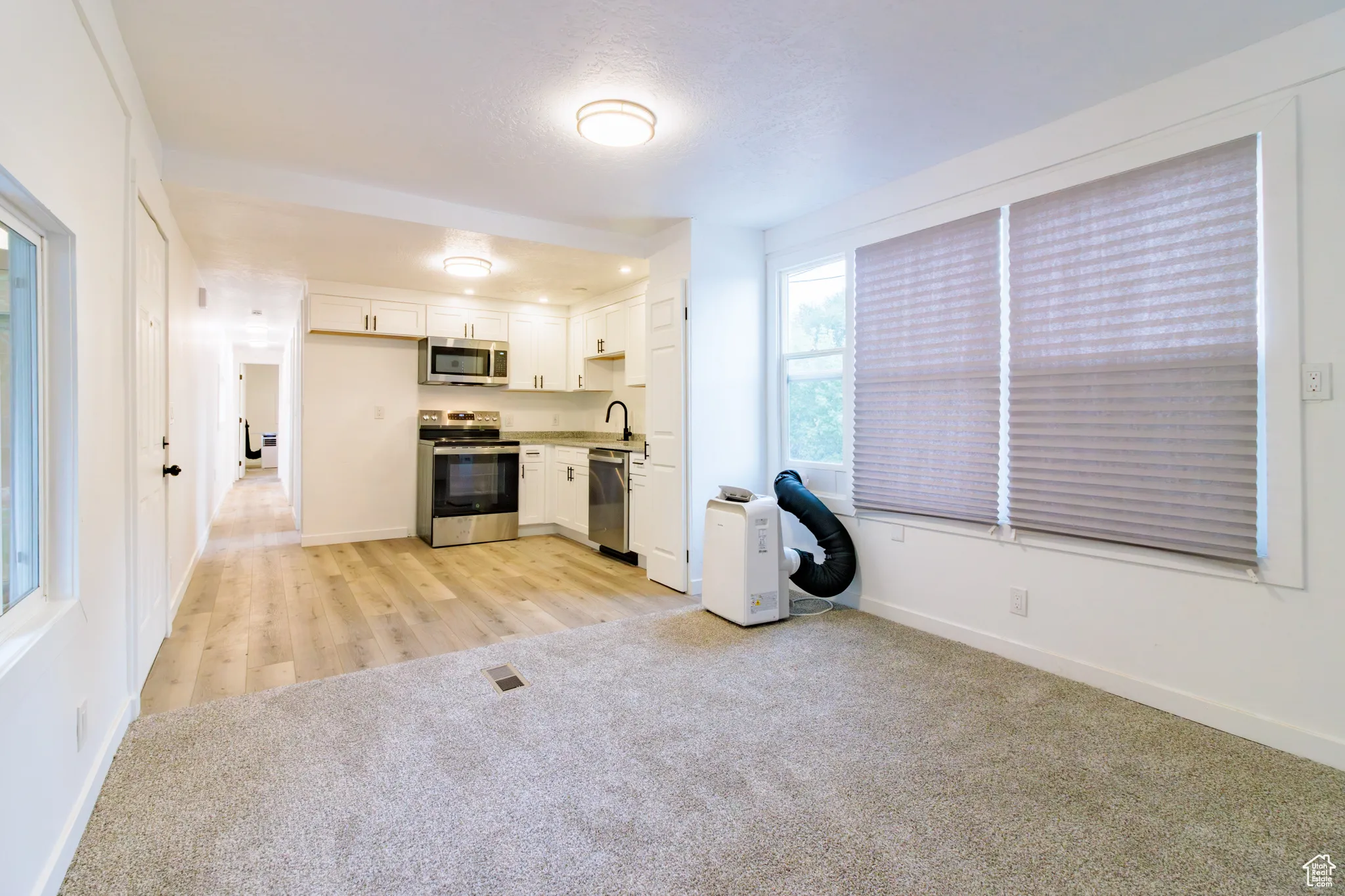 Kitchen featuring light carpet, light countertops, white cabinetry, appliances with stainless steel finishes, and a textured ceiling