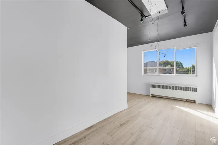 Rentable office featuring radiator, light wood-style flooring, and track lighting