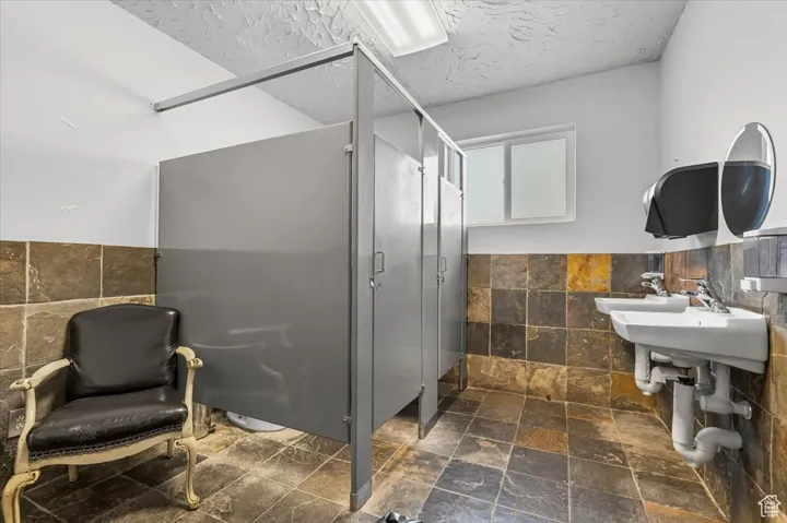 Full bathroom featuring tile walls, a wainscoted wall, stone tile flooring, a textured ceiling, and a stall shower