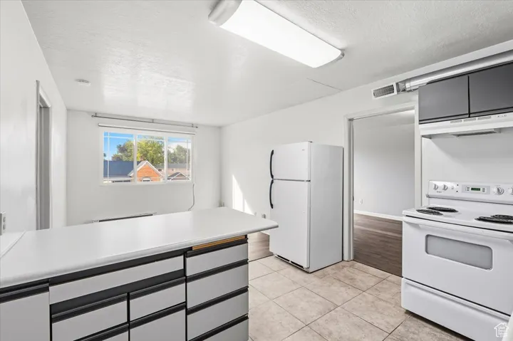 Kitchen with white appliances, a textured ceiling, light countertops, under cabinet range hood, and light tile patterned floors