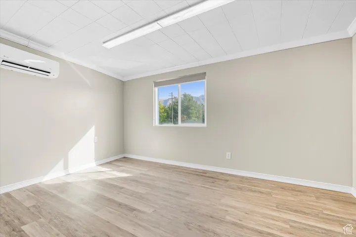 Unfurnished room featuring crown molding, light wood-style floors, and a wall mounted AC