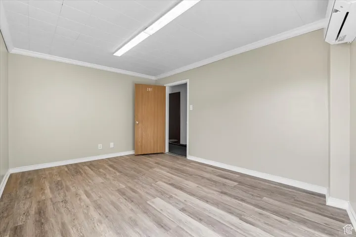 Spare room with ornamental molding, a wall unit AC, and light wood-type flooring