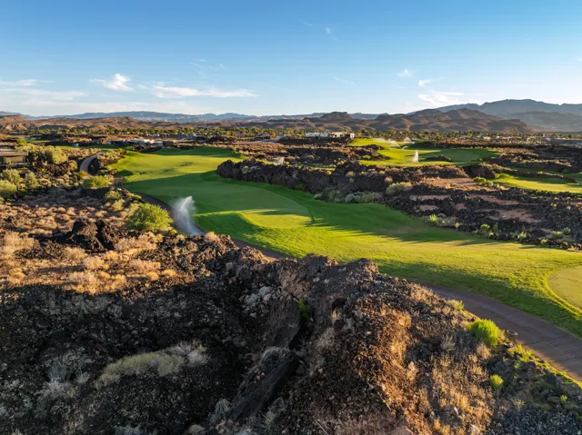 Expansive golf course with manicured greens, surrounded by natural rock formations and distant mountains