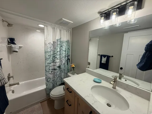Bathroom with shower / bathtub combination with curtain, a textured ceiling, vanity, and dark wood-style flooring