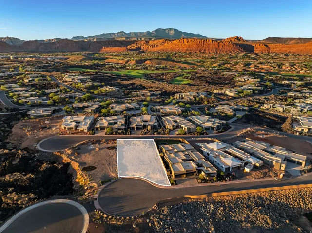 Developable lot with a clear building envelope, surrounded by modern residences and natural desert landscaping, featuring paved roads and distant red rock formations