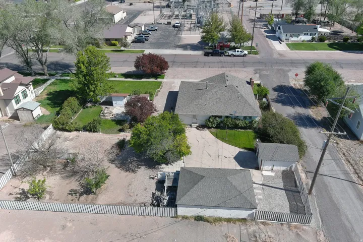 Overhead property view featuring a main residence with a gray shingle roof, a detached garage with a matching shingle roof, a paved driveway, and a fenced yard with mature trees and a lawn area
