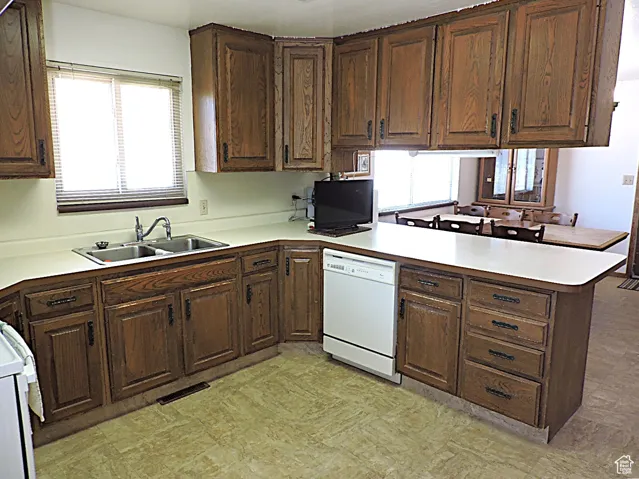 Kitchen featuring a peninsula, light countertops, white appliances, and dark brown cabinetry