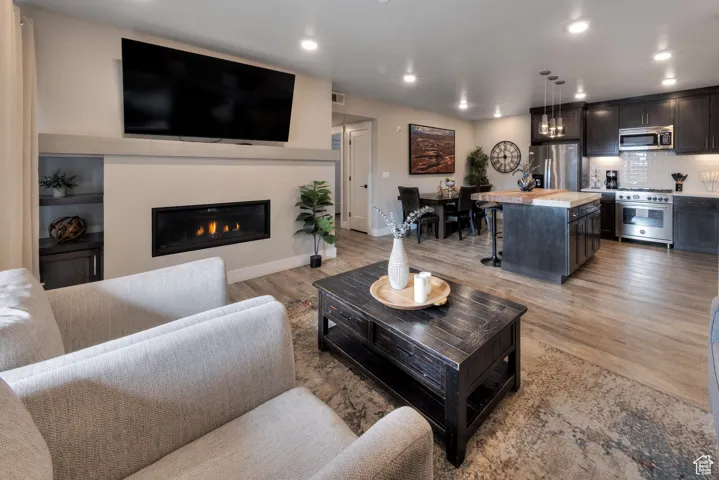 Living room with light wood-style flooring, recessed lighting, and a glass covered fireplace