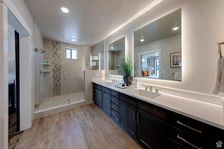 Bathroom with double vanity, a shower stall, light wood-style flooring, ensuite bathroom, and recessed lighting