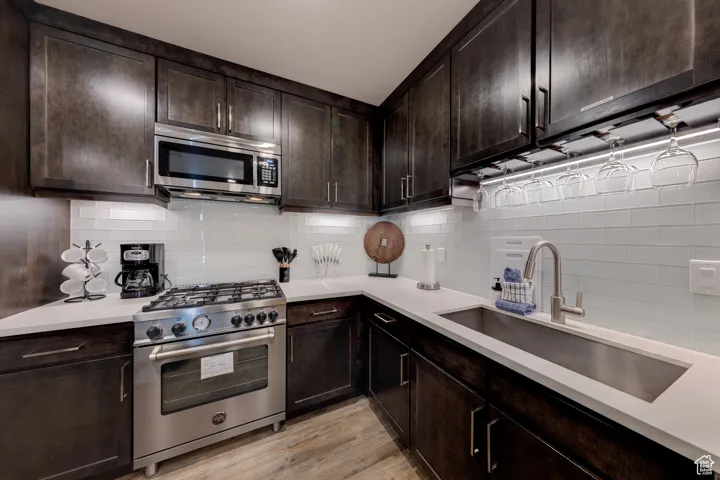 Kitchen featuring dark brown cabinets, stainless steel appliances, tasteful backsplash, and light stone counters