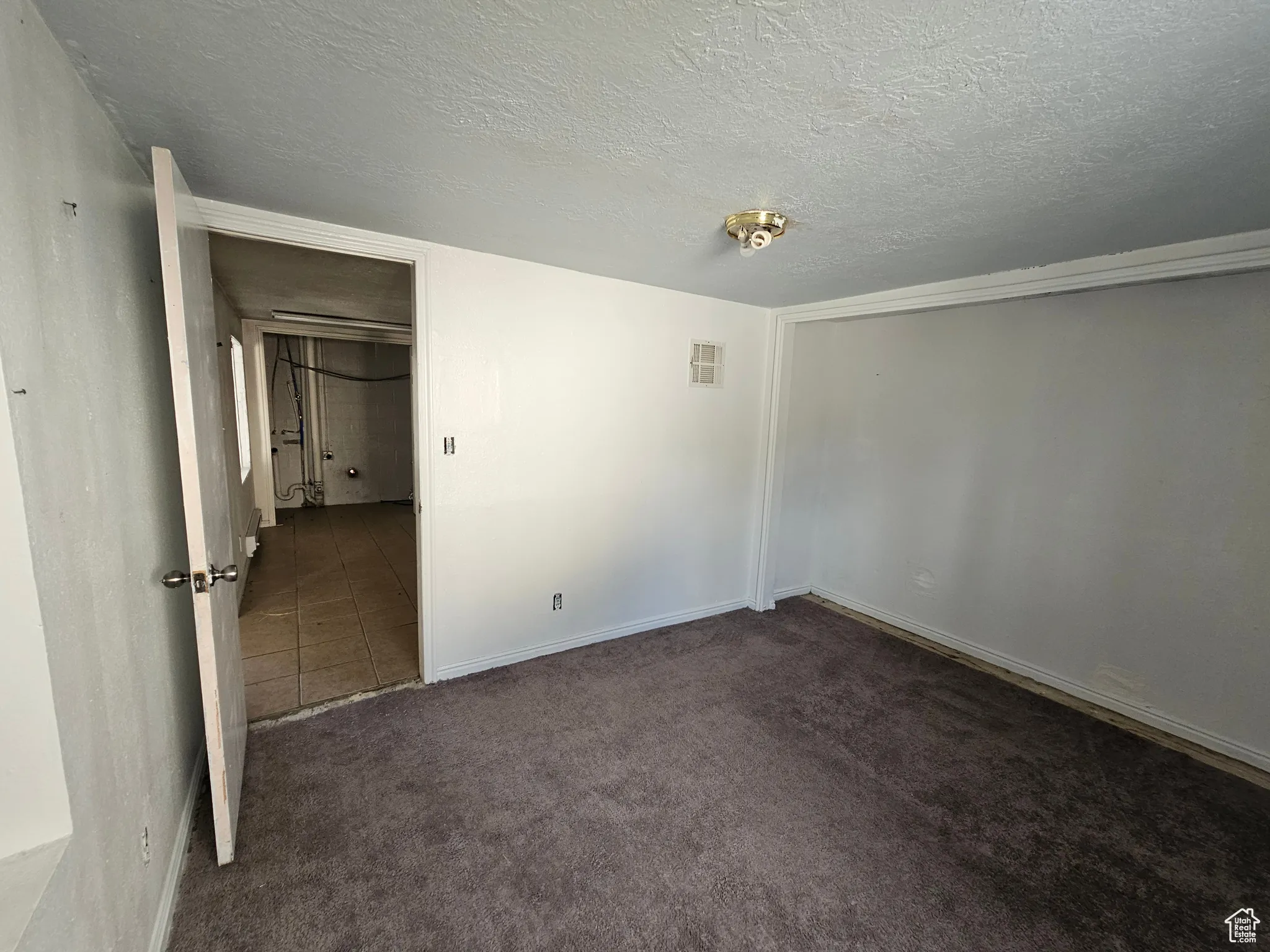 Unfurnished bedroom featuring a textured ceiling, dark colored carpet, and dark tile patterned flooring