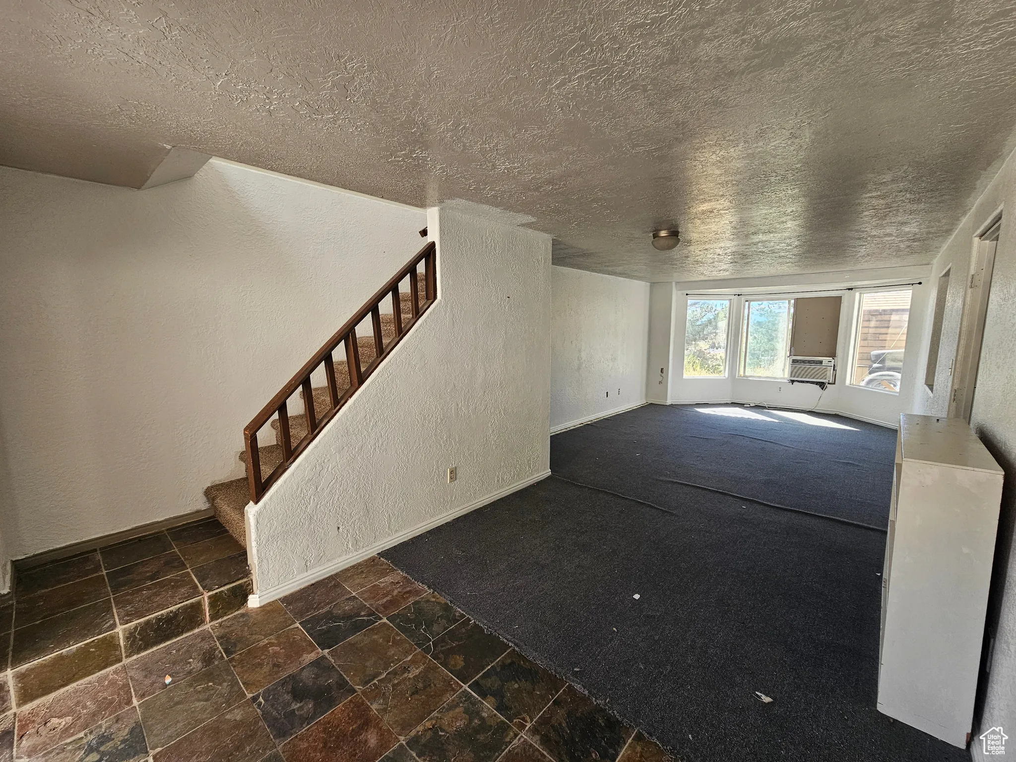 Main entrance, unfurnished living room featuring a textured wall, stone tile floors, stairs, and a textured ceiling
