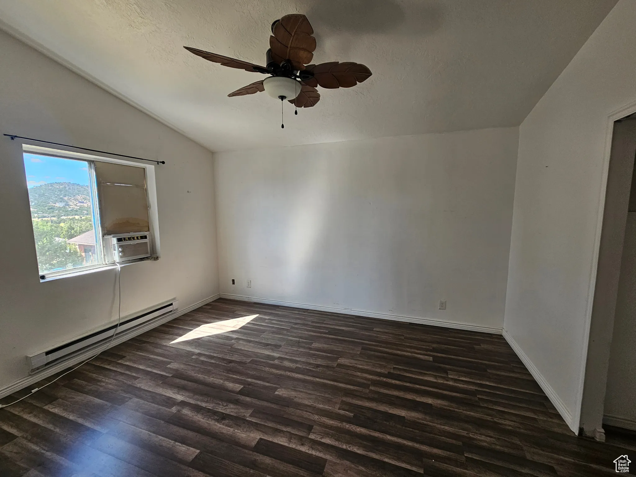Spare room with baseboard heating, vaulted ceiling, dark wood-type flooring, a textured ceiling, and a ceiling fan