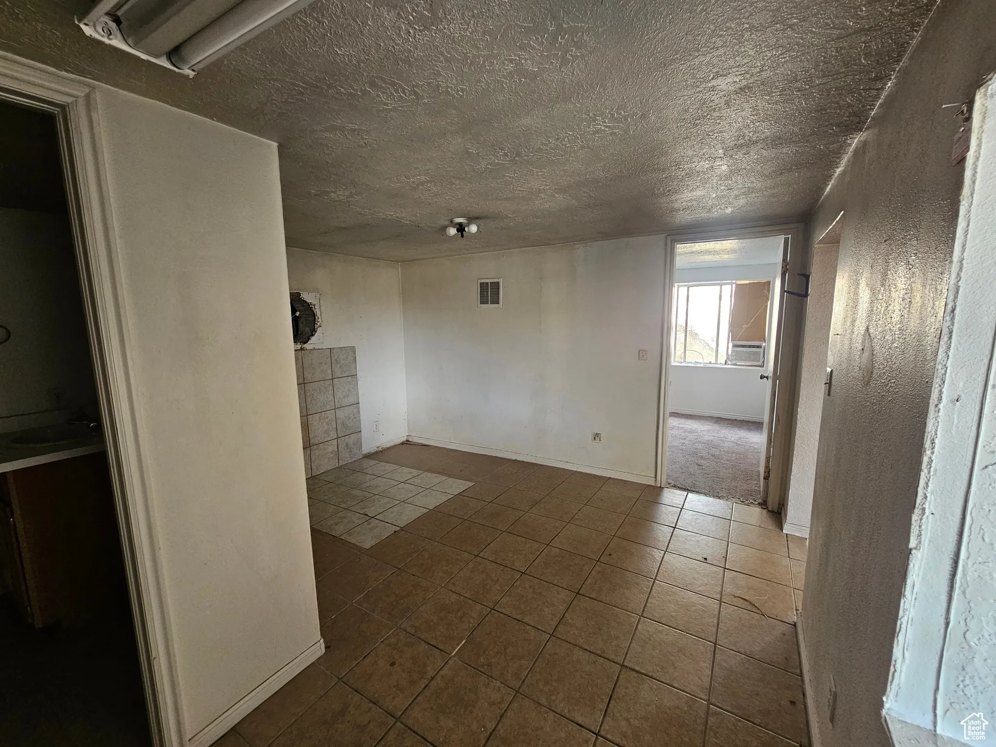 Tiled empty room featuring a textured wall and a textured ceiling