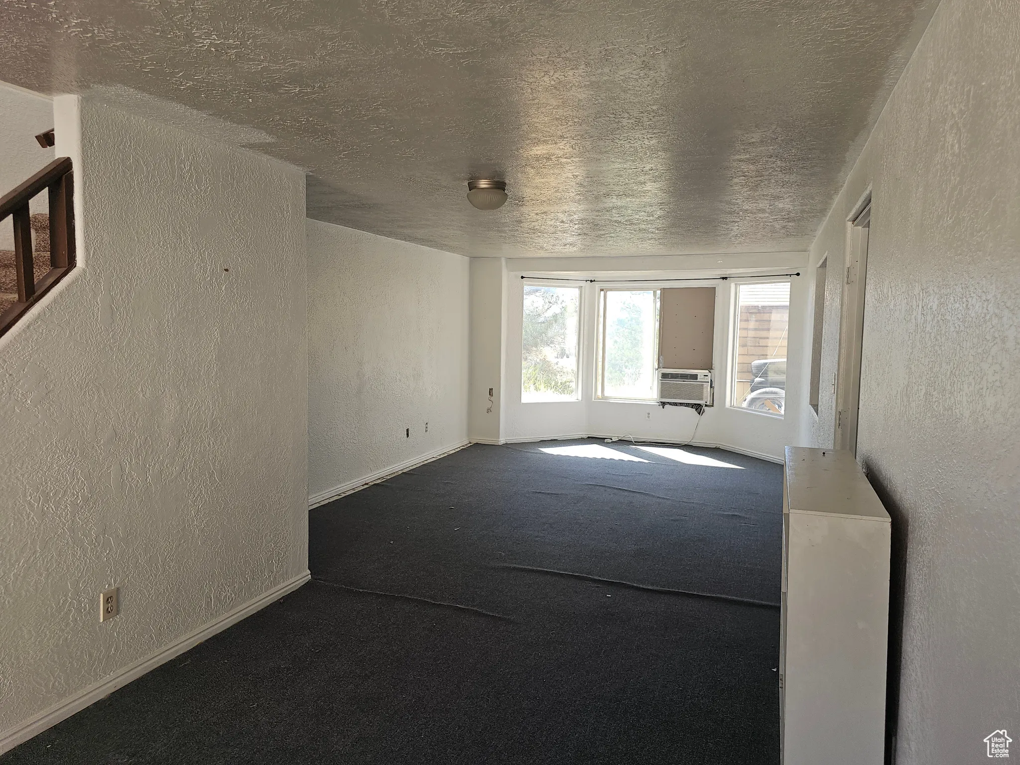 Unfurnished living room featuring a textured wall, a textured ceiling, dark carpet, and cooling unit