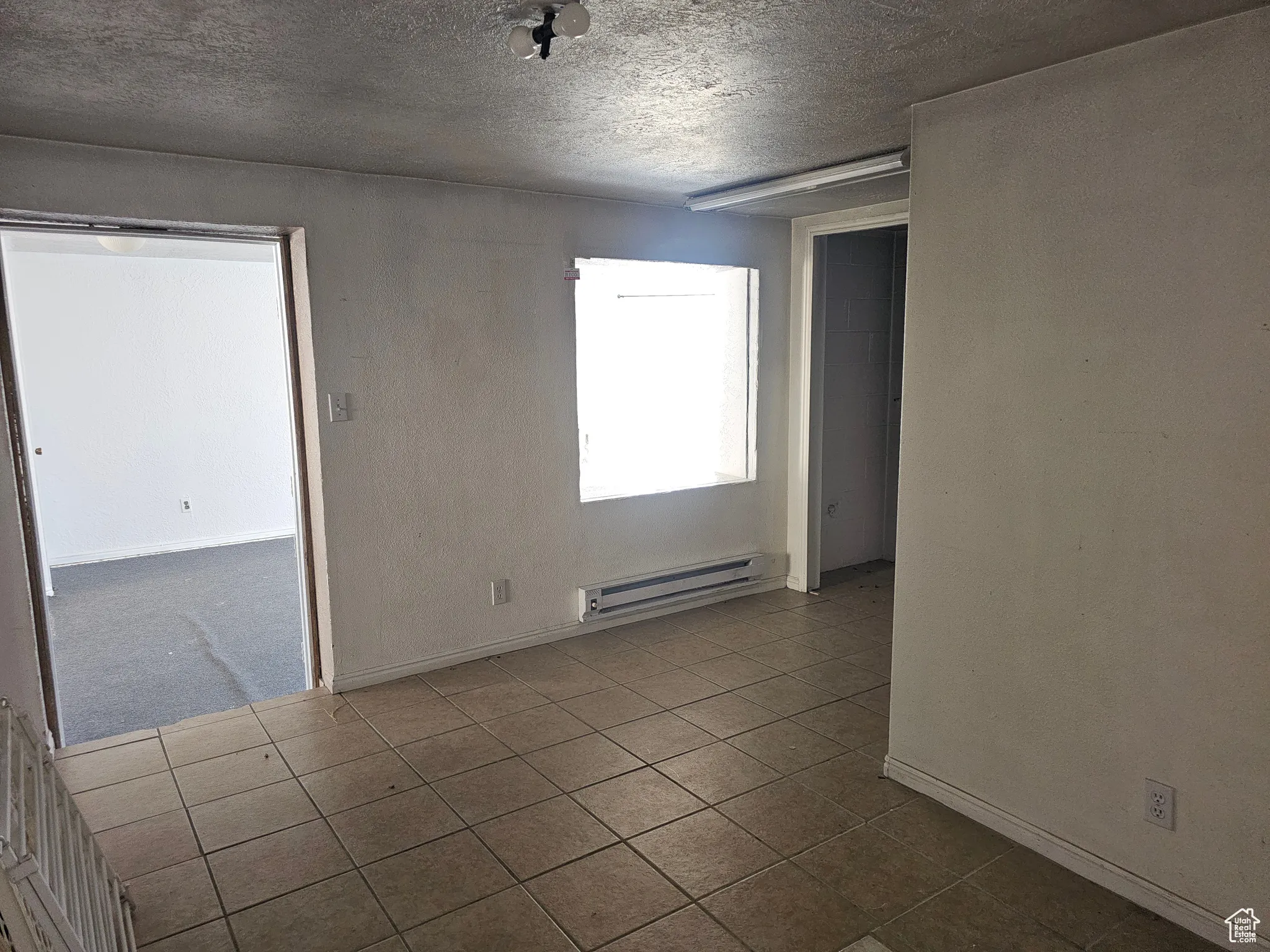 Unfurnished room with a textured ceiling, dark tile patterned flooring, baseboard heating, and a textured wall