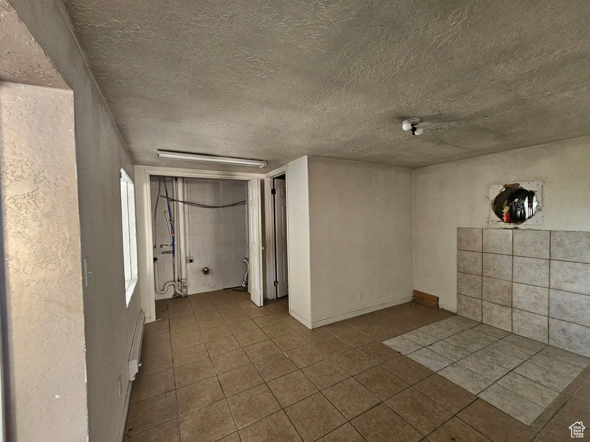 Empty room featuring tile patterned floors, a baseboard heating unit, and a textured ceiling