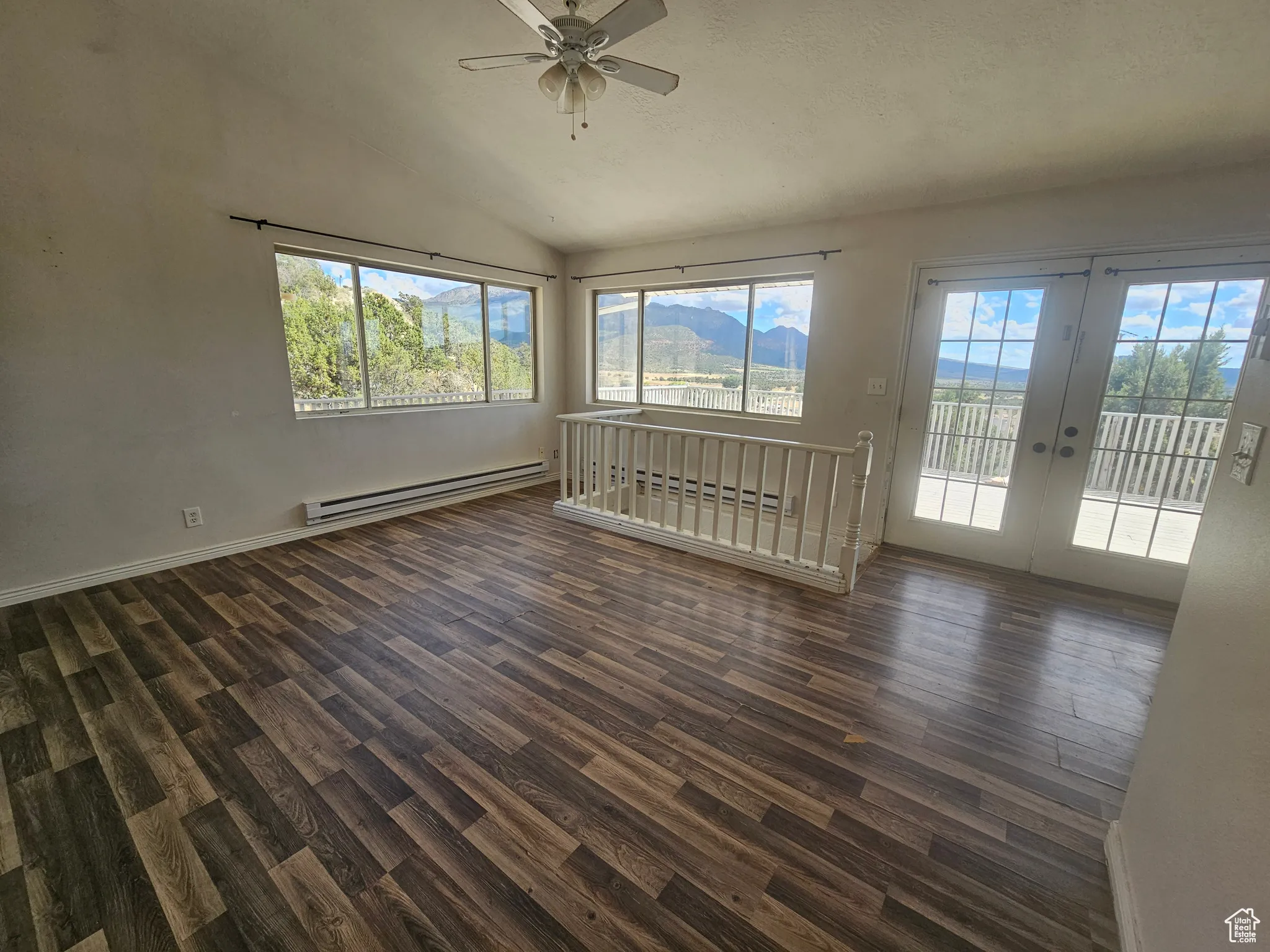 Unfurnished living room with vaulted ceiling, baseboard heating, dark wood finished floors, a mountain view, and ceiling fan