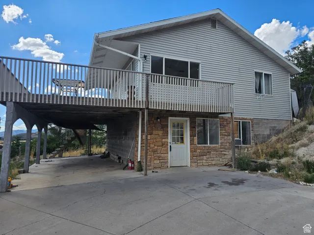 View of front facade with concrete driveway, stone siding, and a wooden deck