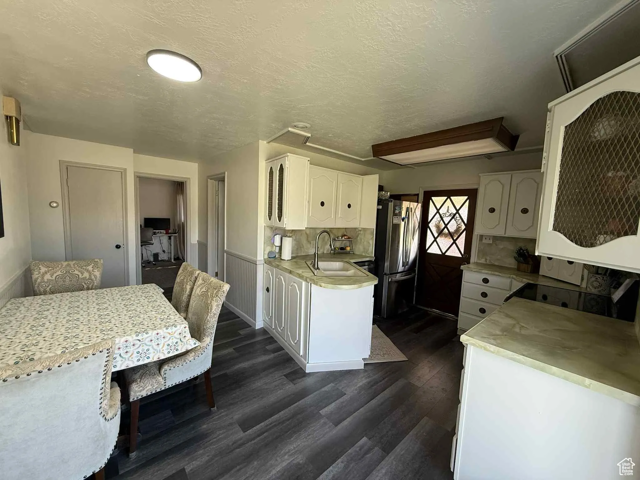 Kitchen and dining area with white cabinetry, light countertops, a textured ceiling, dark wood finished floors, and freestanding refrigerator