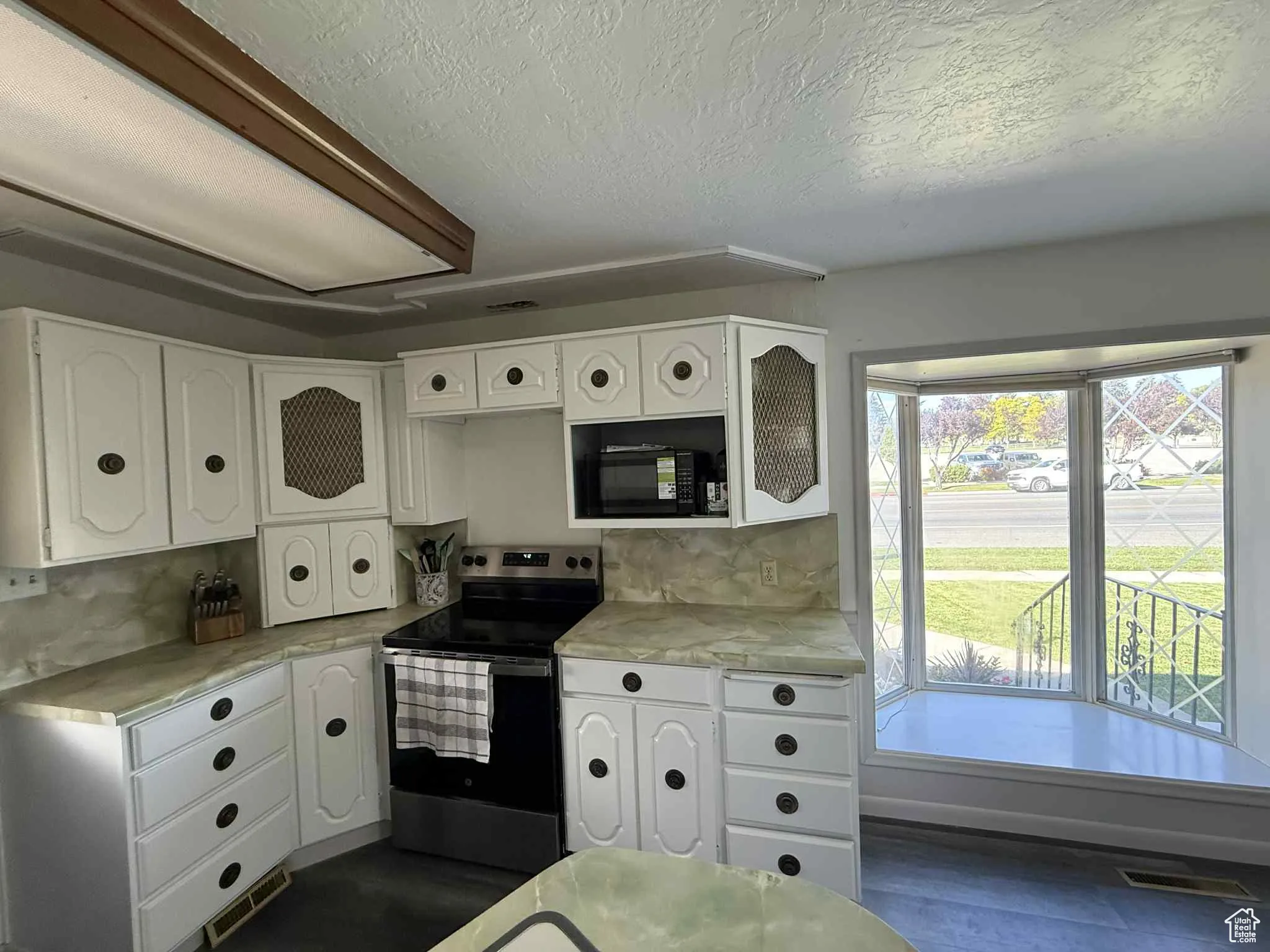 Kitchen featuring all new appliances as of 2024,  white cabinetry, stainless steel range with electric cooktop, light countertops, and a textured ceiling