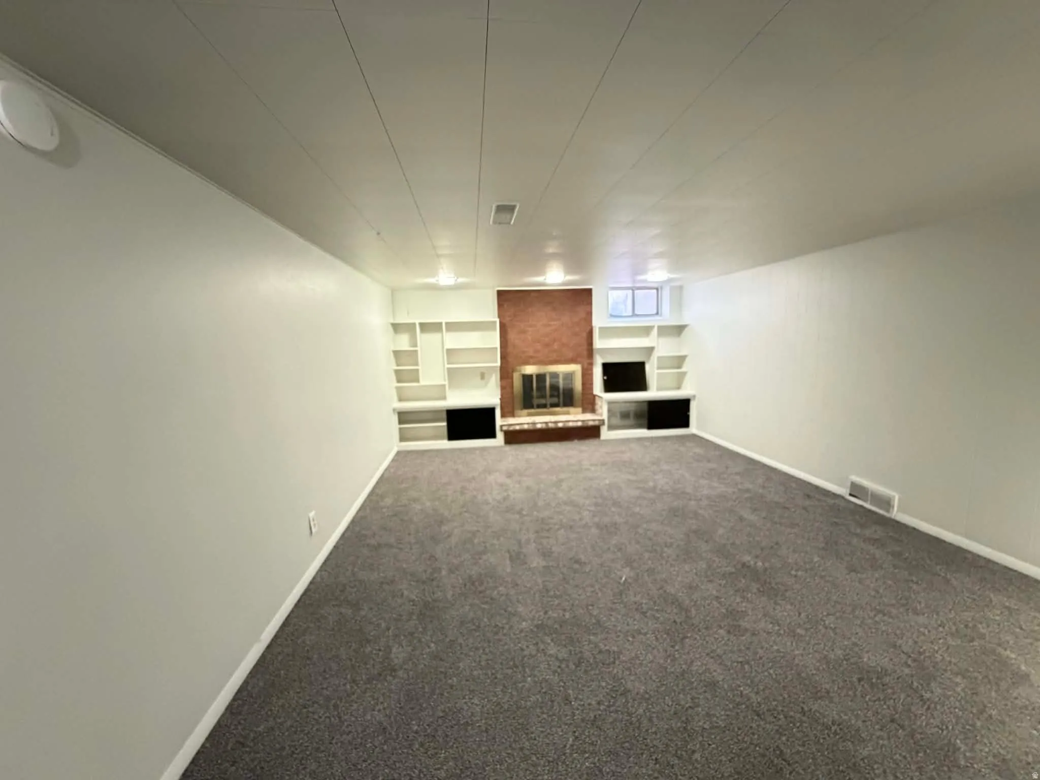 Unfurnished living room featuring built in shelves, a brick fireplace, and dark carpet