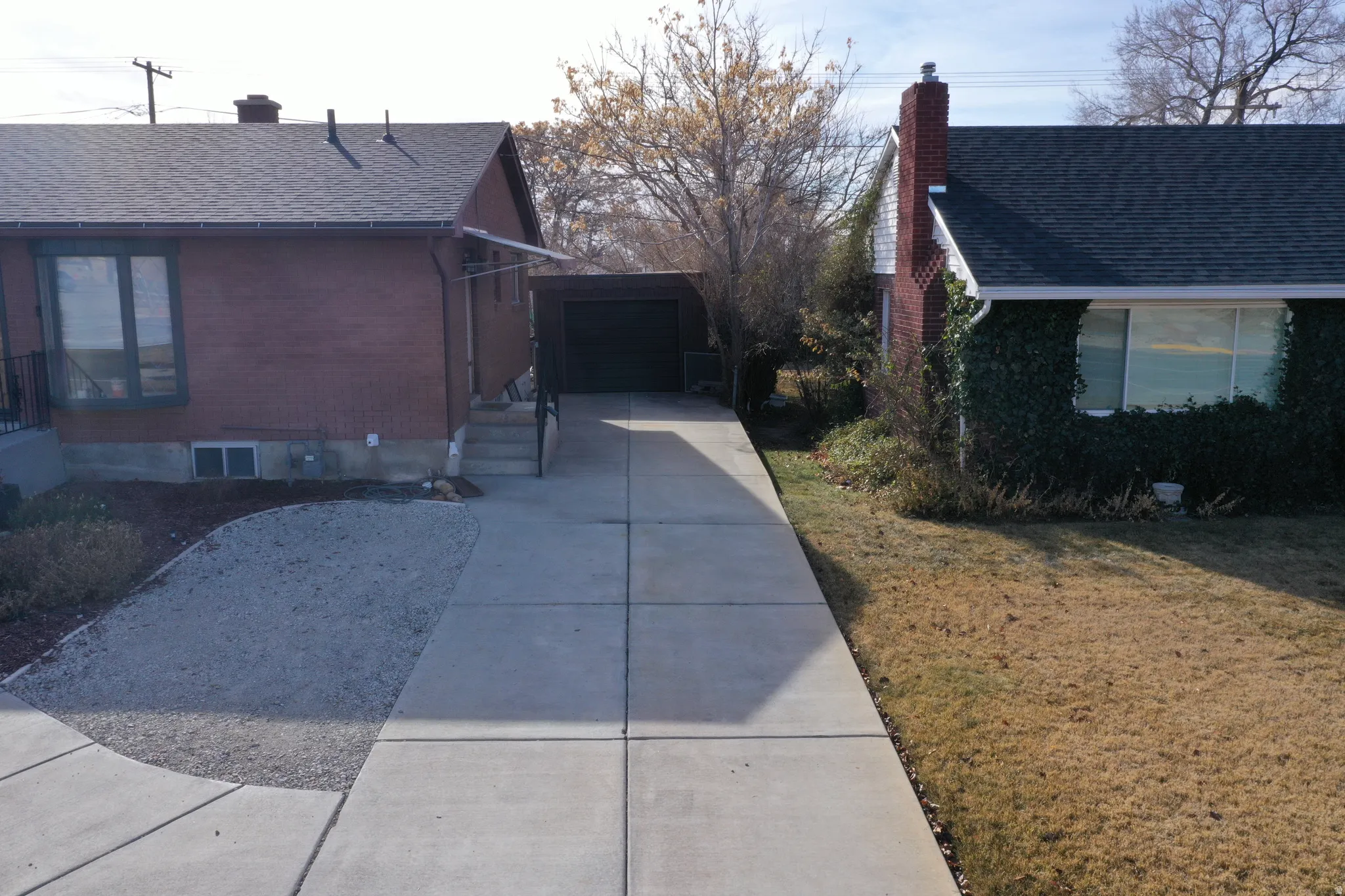 View of property exterior with brick siding, a chimney, roof with shingles, driveway, and an outdoor structure