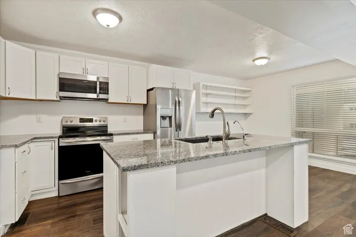 Kitchen with open shelves, stainless steel appliances, light stone countertops, a textured ceiling, and dark wood-style flooring