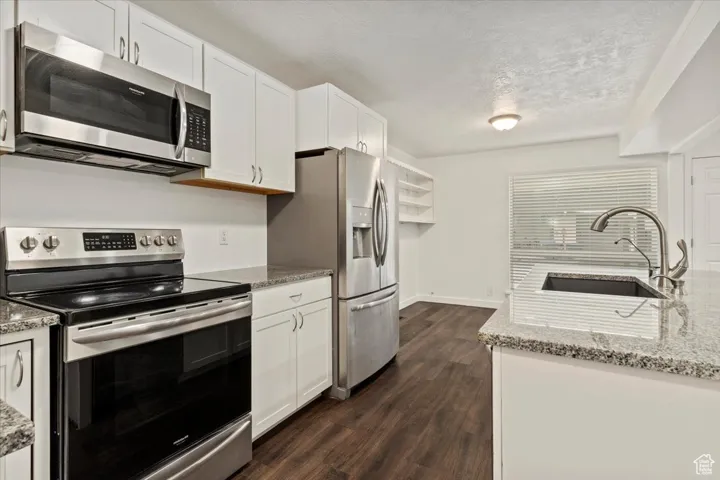 Kitchen with stainless steel appliances, light stone countertops, white cabinets, dark wood-style floors, and a textured ceiling