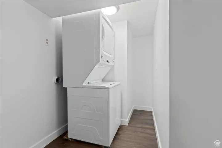 Laundry area with stacked washer and clothes dryer and dark wood-style floors