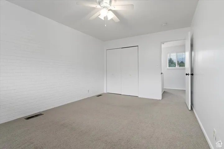 Unfurnished bedroom with carpet floors, ceiling fan, a closet, and brick wall