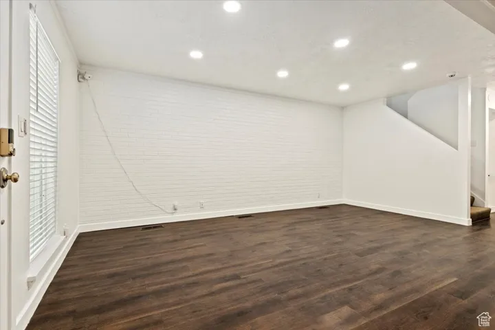 Below grade area with dark wood-style floors, recessed lighting, stairway, and brick wall