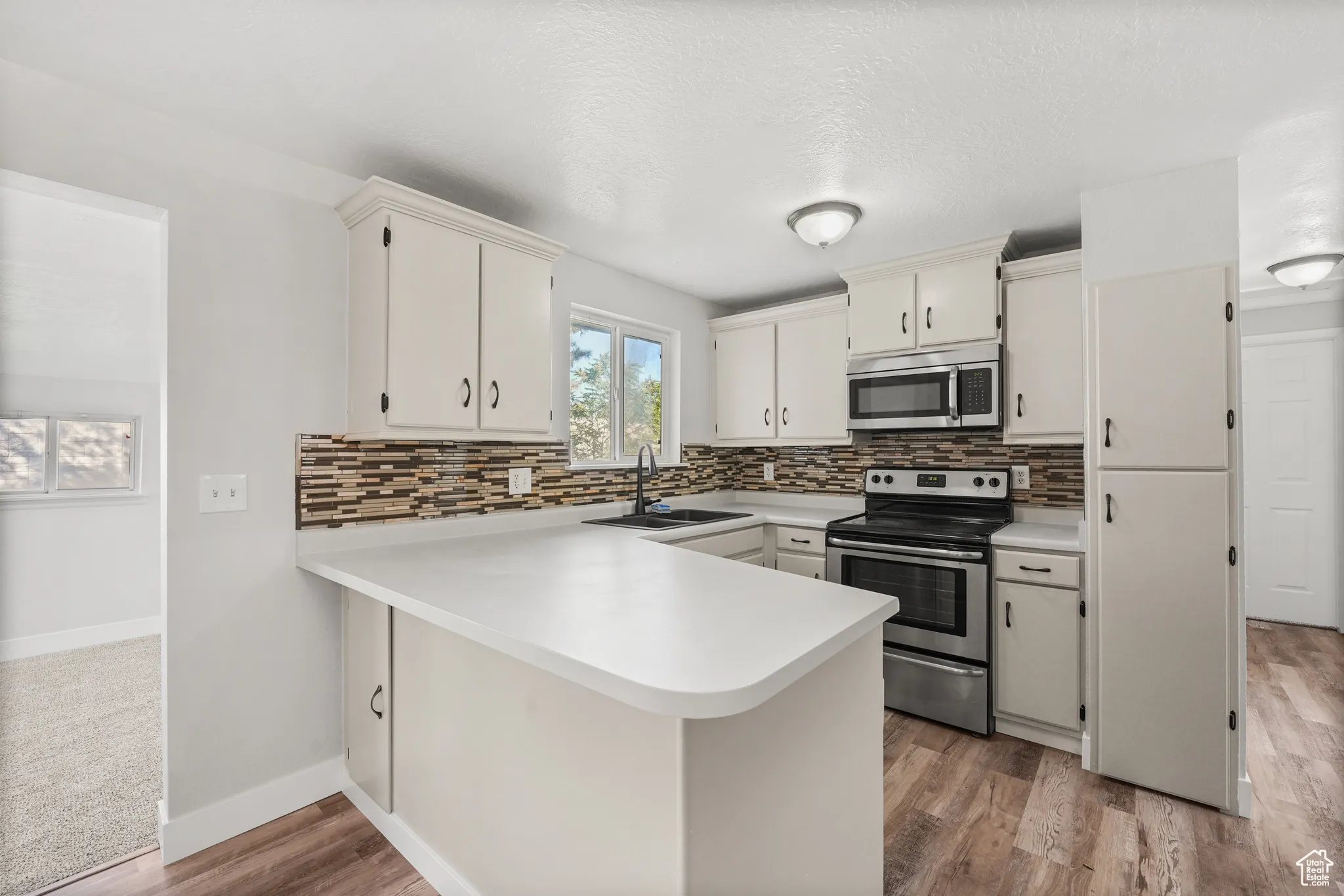 Kitchen with light countertops, appliances with stainless steel finishes, a peninsula, decorative backsplash, and a textured ceiling