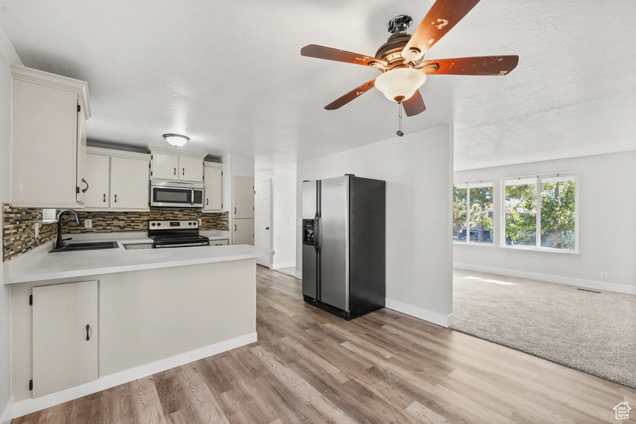 Kitchen featuring appliances with stainless steel finishes, light countertops, open floor plan, decorative backsplash, and a peninsula