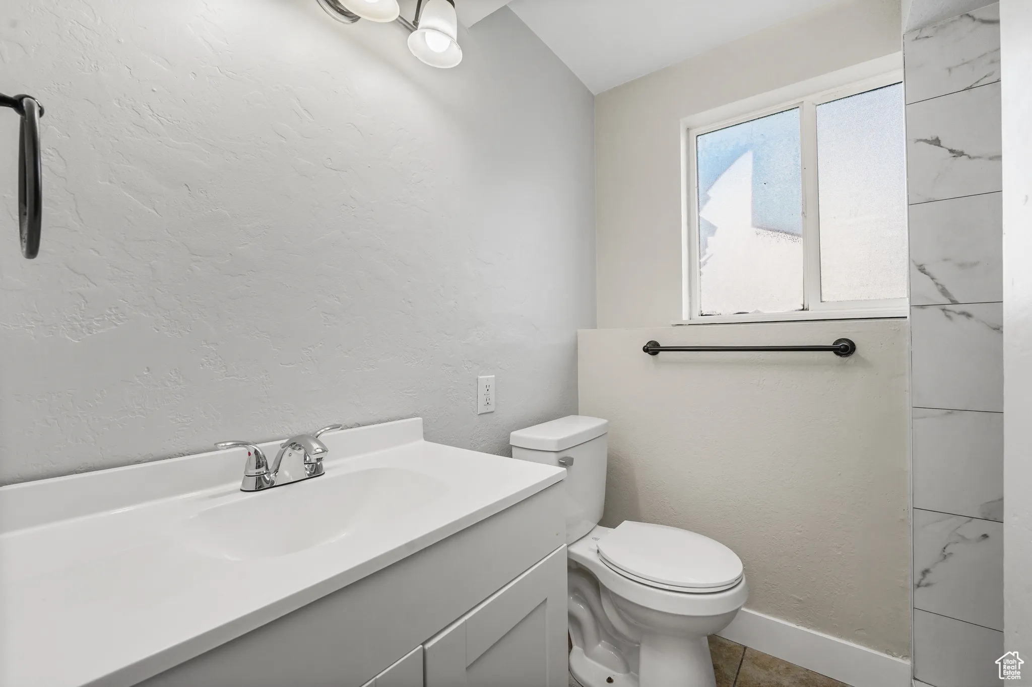Full bathroom with a textured wall, vanity, and light tile patterned flooring