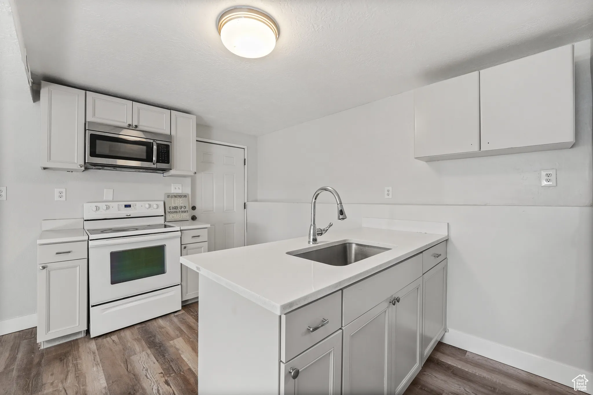 Kitchen with electric stove, stainless steel microwave, a peninsula, dark wood-style floors, and white cabinetry