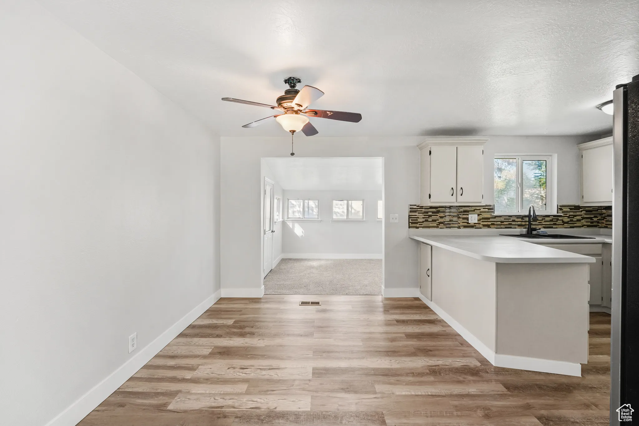 Kitchen with a peninsula, light countertops, backsplash, light wood finished floors, and a ceiling fan