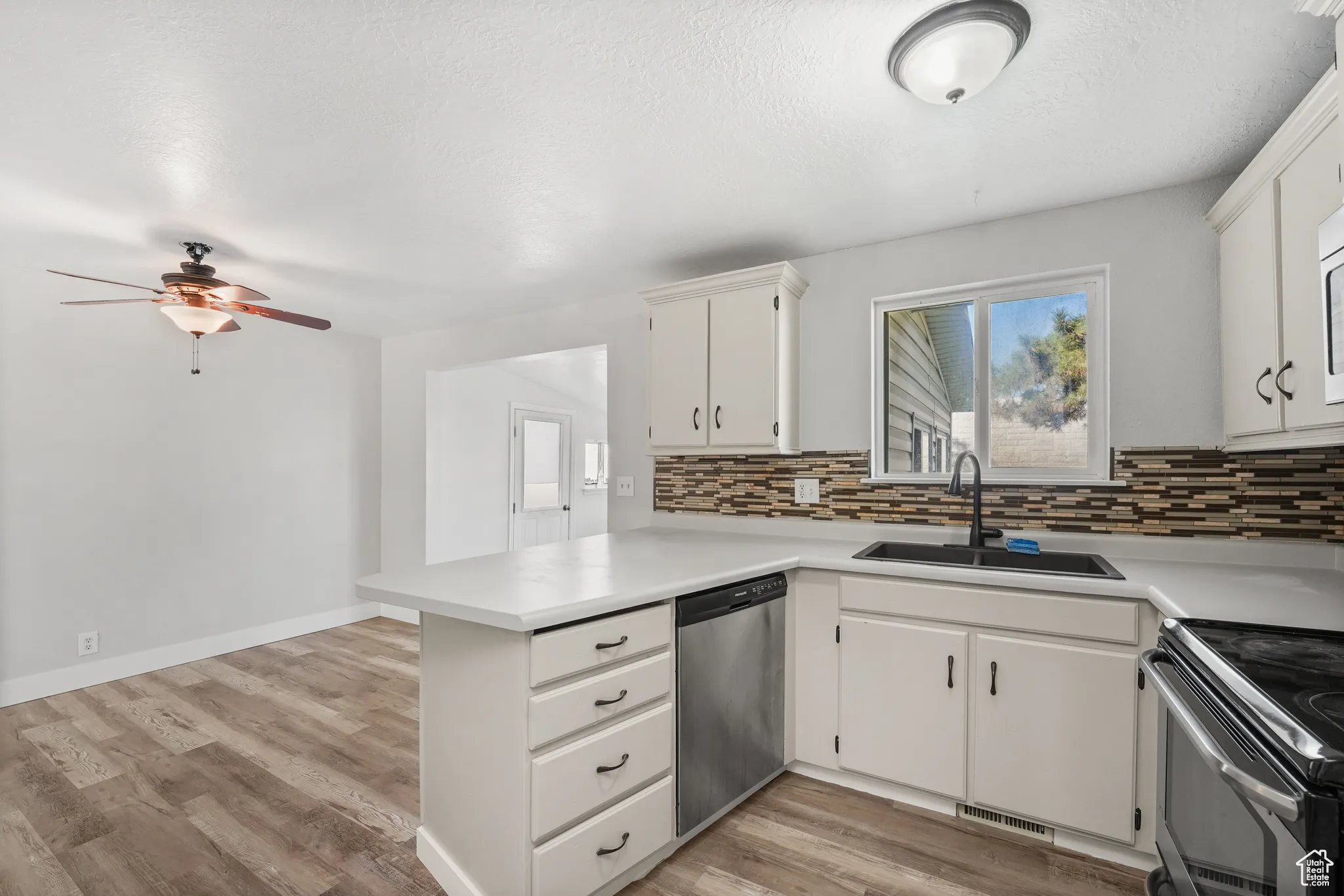 Kitchen with light countertops, a peninsula, white cabinets, stainless steel appliances, and light wood-style flooring