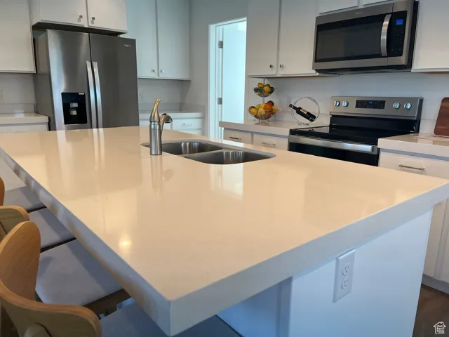 Kitchen featuring appliances with stainless steel finishes, an island with sink, a breakfast bar area, and white cabinetry