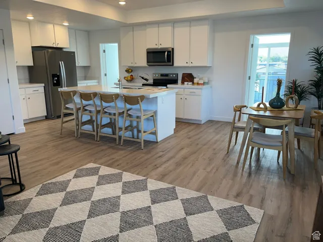 Kitchen with light countertops, a kitchen breakfast bar, a tray ceiling, white cabinets, and recessed lighting