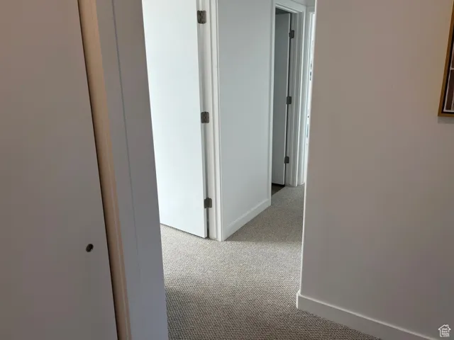 Corridor featuring light colored carpet and baseboards