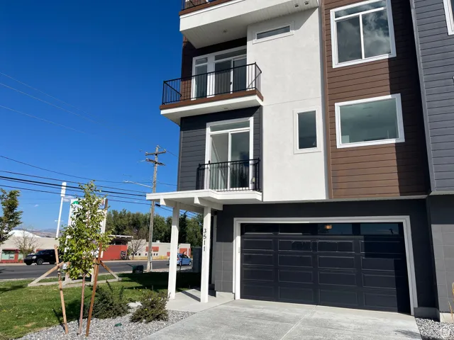 Modern home with a balcony, an attached garage, driveway, and stucco siding