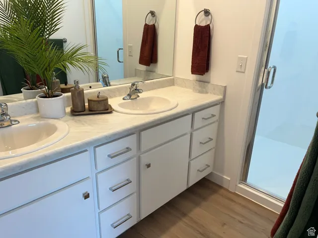 Full bathroom with a shower stall, double vanity, and light wood-style flooring