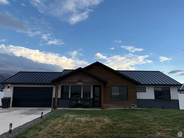 View of front of home featuring a metal roof, an attached garage, a front yard, and driveway