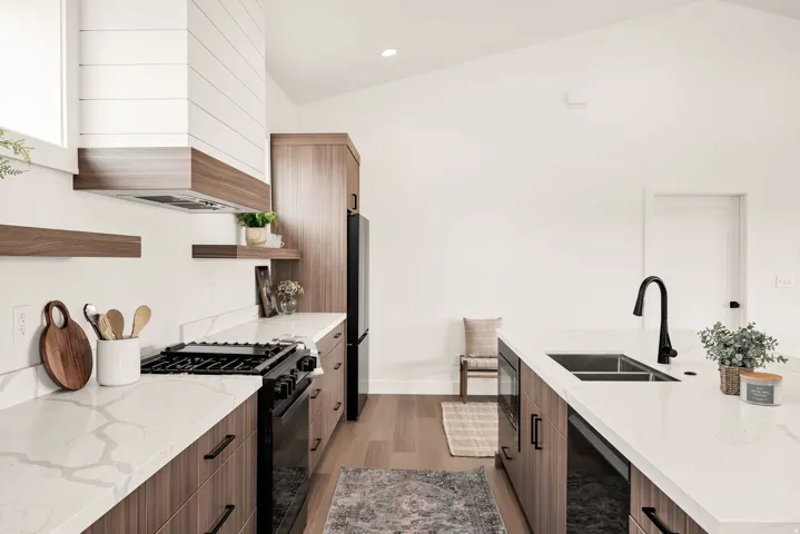 Kitchen with open shelves, modern cabinets, black appliances, light stone countertops, and vaulted ceiling