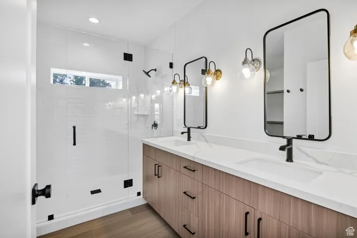 Bathroom with double vanity, a stall shower, dark wood-type flooring, and recessed lighting