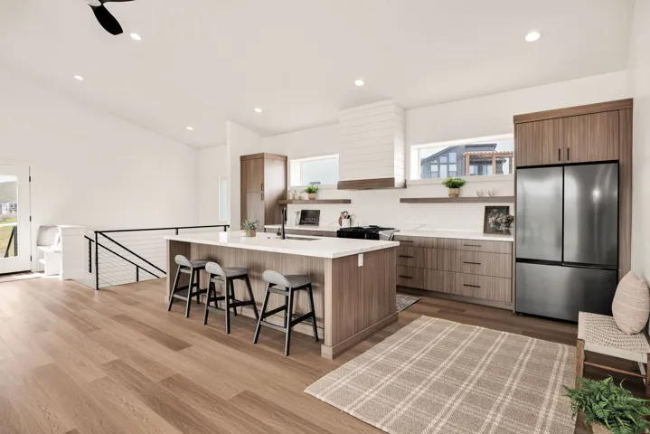Kitchen with freestanding refrigerator, an island with sink, a breakfast bar area, modern cabinets, and dark wood-style flooring
