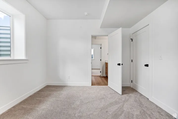 Unfurnished bedroom with light colored carpet and baseboards