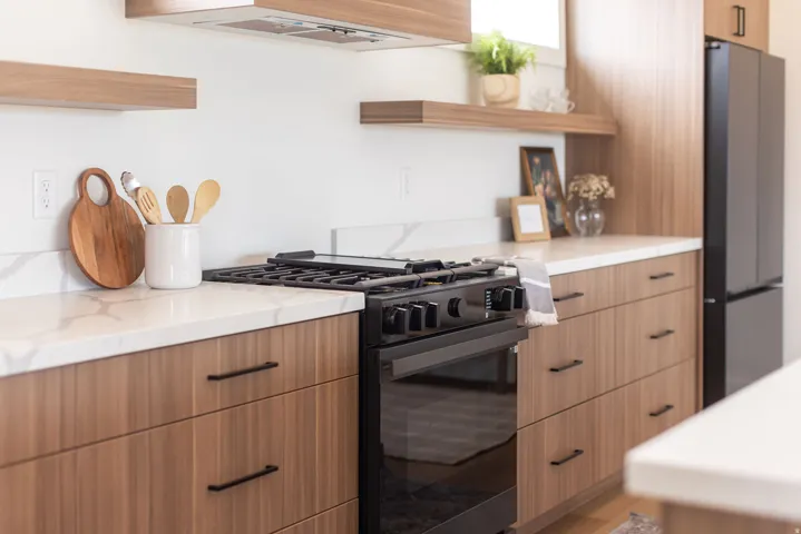 Kitchen with open shelves, gas stove, modern cabinets, freestanding refrigerator, and light stone countertops