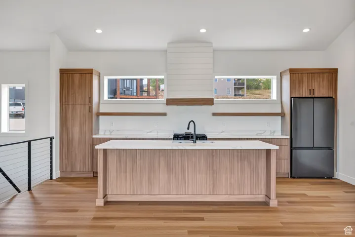 Kitchen with open shelves, freestanding refrigerator, recessed lighting, light stone countertops, and light wood-style flooring